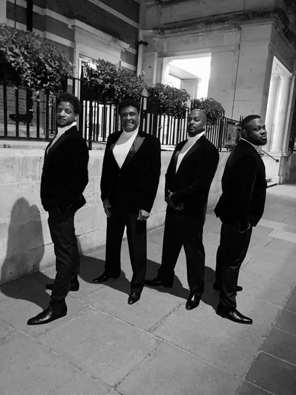 Black and White image of four black men in suits looking into the camera 