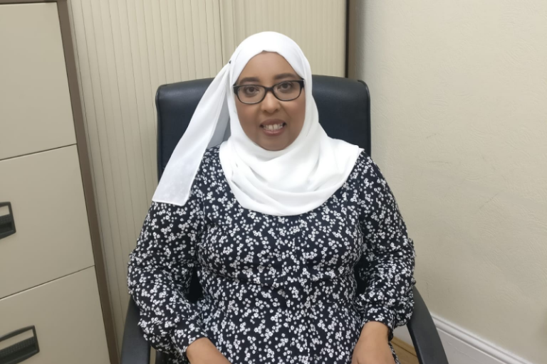 Black woman, who is wearing a hijab sitting in a chair looking into the amera