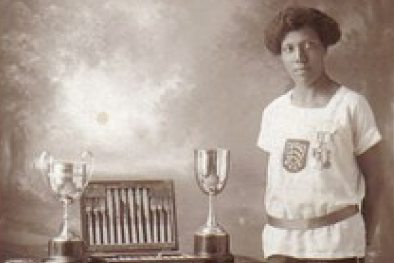 Old photograph of a black woman standing next to a large amount of trophies